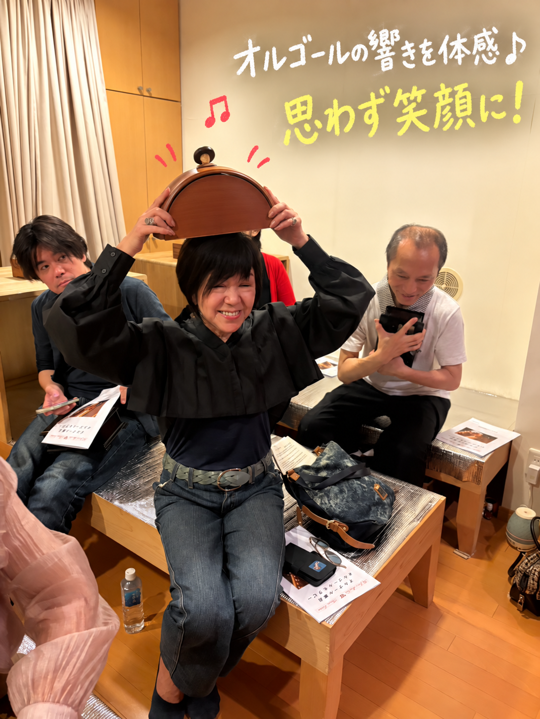 オルゴールを頭の上にのせて笑顔で響きを体験する参加者の写真に、オルゴールの響きを体感、思わず笑顔にと記した画像