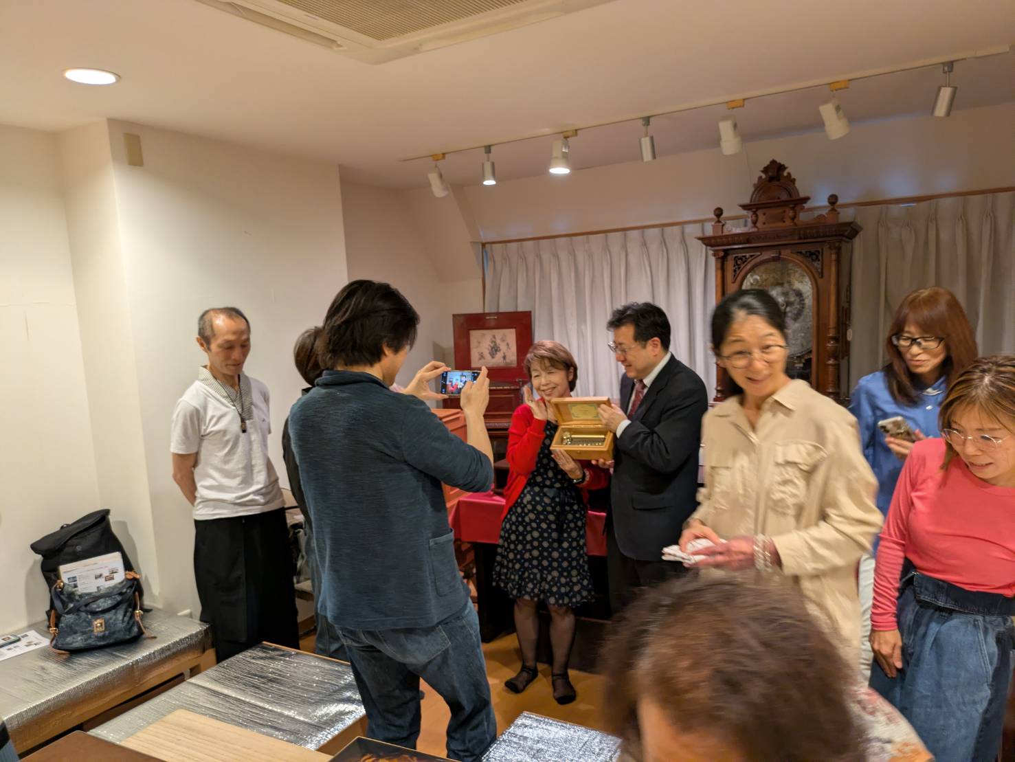 購入したオルゴールを持つ畑中先生と佐伯一成さんを参加者が撮影する様子